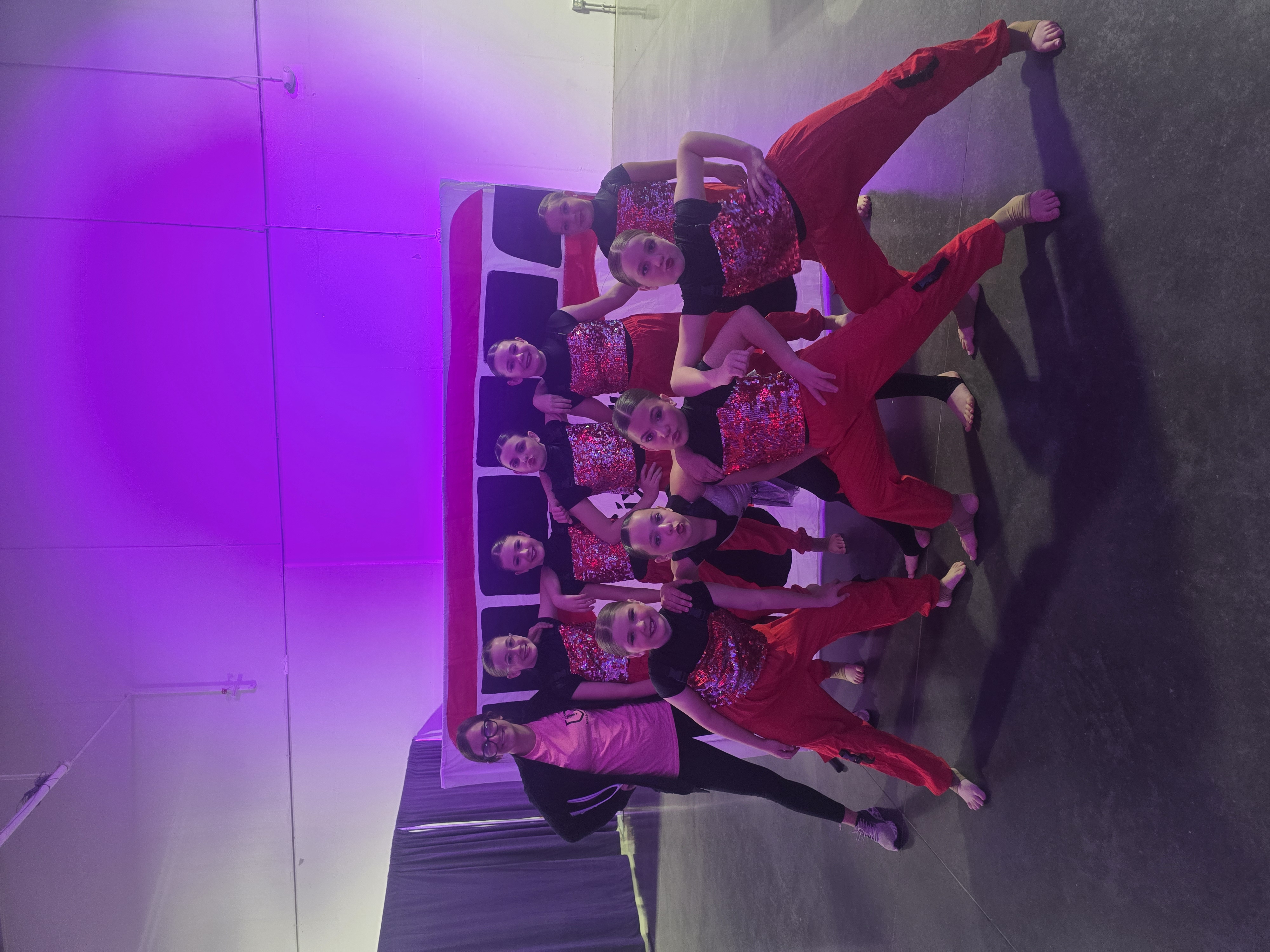 Inspirations Academy dancers backstage in red and black costumes with their instructor before a competition performance.