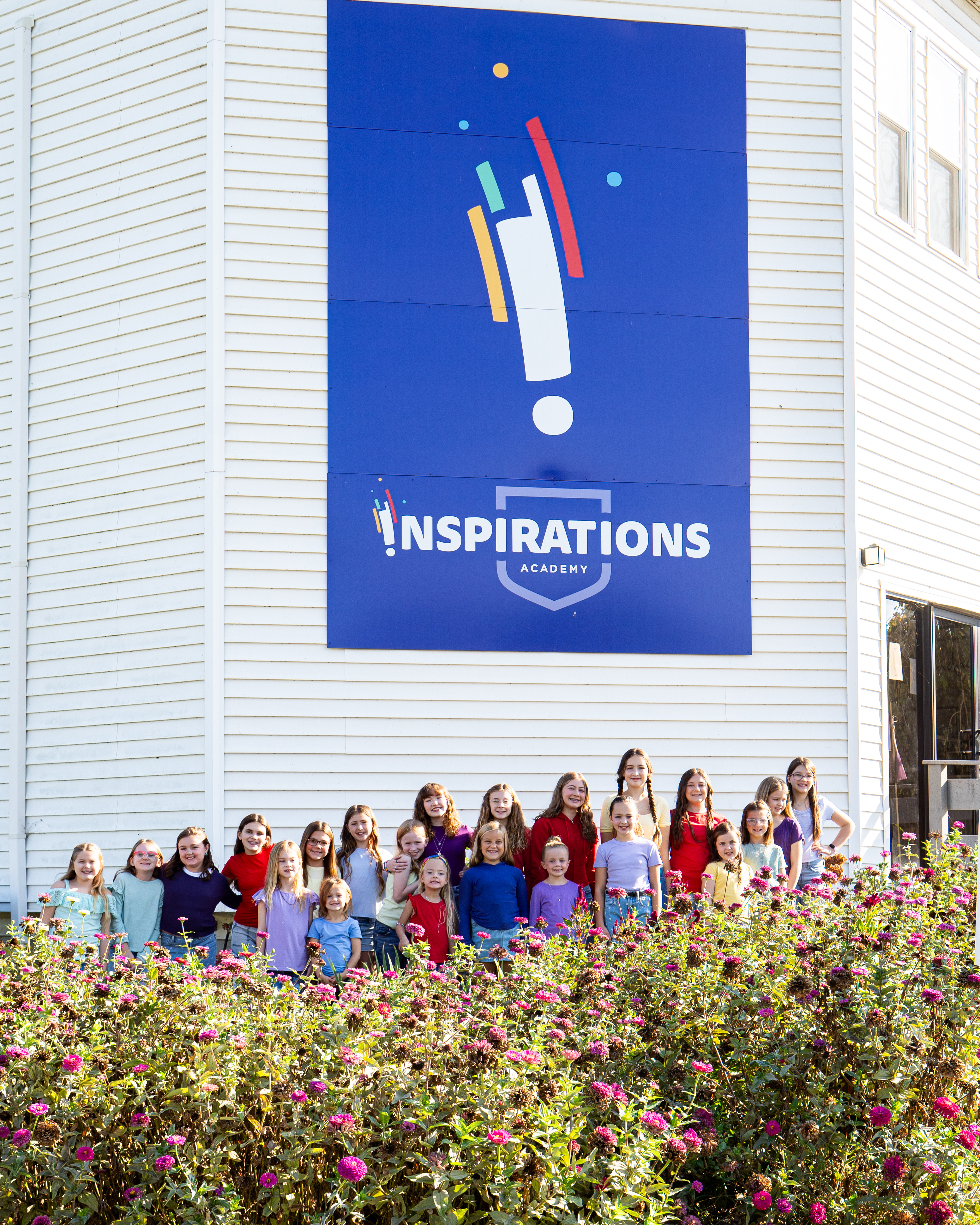 A group of Inspirations Academy students posing in front of the studio's exterior sign.