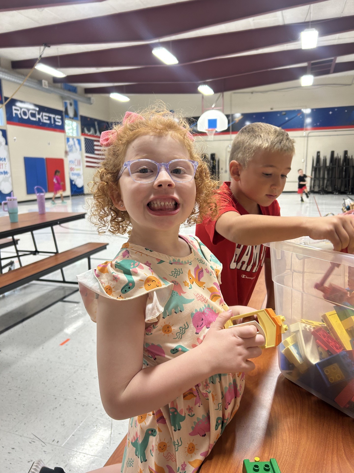 A student smiling while playing with toys during Inspirations Academy after school care in the school gym