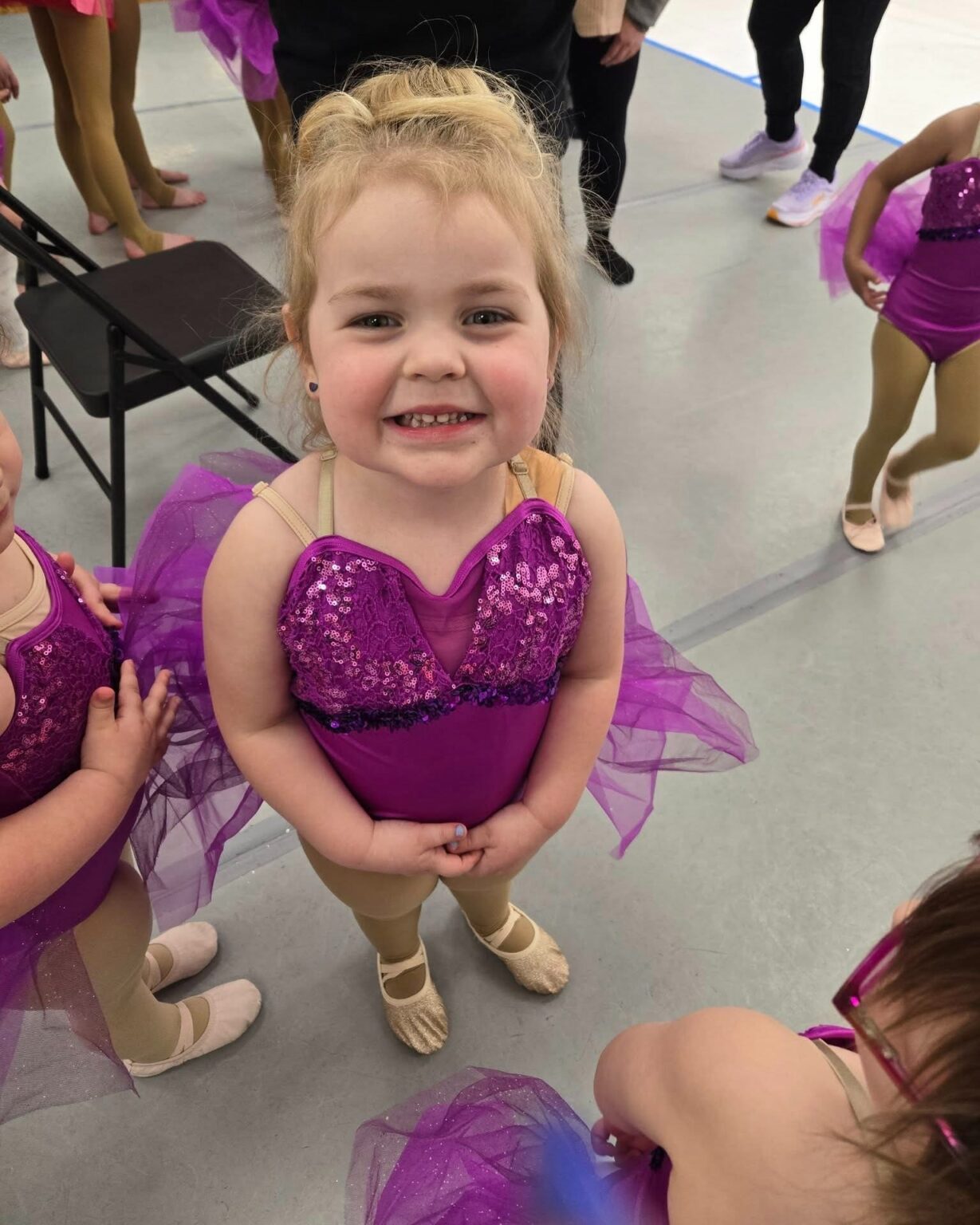 A young dancer in a purple sequinned costume smiling before a recital at Inspirations Academy